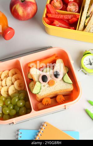 Lunchboxen mit Snacks, einer Flasche Saft, Wecker und Schreibwaren auf weißem Tisch Stockfoto