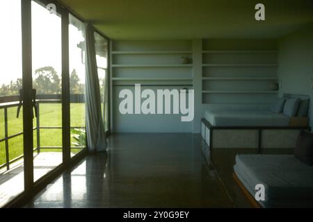Tabanan, Bali, Indonesien - 26. August 2024: Schlafzimmer mit eingebauten Regalen, einem kompakten Bett und raumhohen Panoramafenstern mit Blick auf die Decke Stockfoto