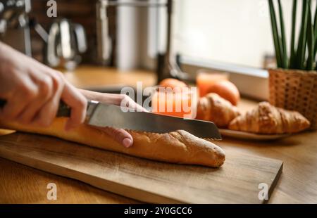 Mädchen handgeschnitten französisches Baguette mit Messer auf einem Brett in der Küche. Leckeres, rustikales, frisches Brot zum Frühstück Stockfoto