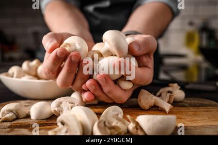 Häuptlingshände halten Schampignons in der Küche. Restaurant-Profi mit essbaren Pilzen aus Holz Stockfoto