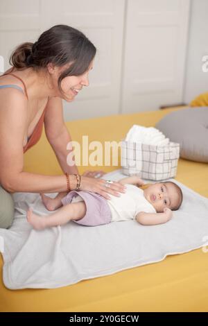 Eine Frau hält ein Baby auf einem Bett, kurz davor, seine Windel zu wechseln. Stockfoto