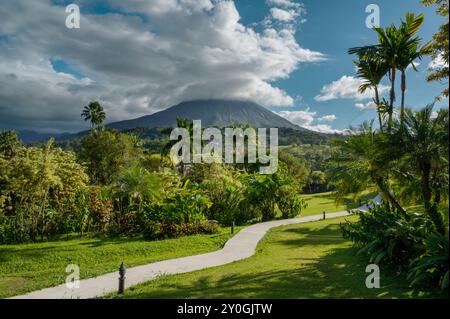 Pfad führt durch grüne Gras tropische Gärten Arenal Vulkan Costa Rica, Mittelamerika. Blauer Himmel mit Wolken. Konzept für tropischen Urlaub. Stockfoto