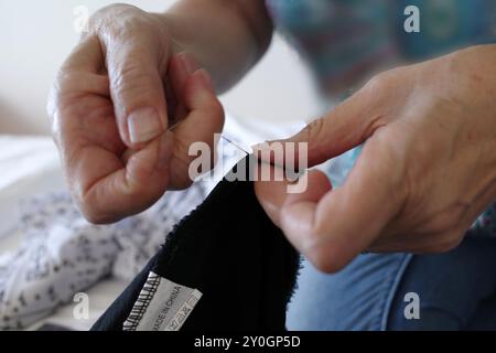 Die Hände einer älteren Frau, die Nadel und Faden benutzt, um ein schwarzes Kleid zu reparieren. Reparieren statt ersetzen Stockfoto