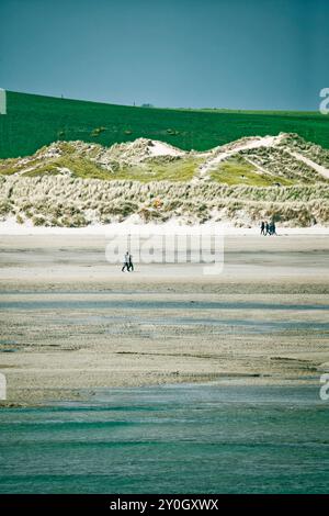 West Cork, Irland, 22. April 2023. Der Sandstrand wird von einer Linie grüner Dünen begrenzt. Ein paar Spaziergänge am Strand entlang. Das Wasser ist ruhig und klar. Stockfoto