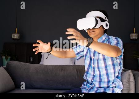 Mit dem VR-Headset sitzt ein asiatischer Mann auf der Couch und erlebt die virtuelle Realität Stockfoto