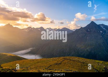 Die Sonne geht über den majestätischen Otztaler Alpen auf und strahlt auf den Gipfeln und Tälern ein goldenes Leuchten aus. Die Wolken hängen sanft über der Landschaft und schaffen bei Sonnenaufgang einen atemberaubenden Kontrast in der ruhigen Bergregion Stockfoto