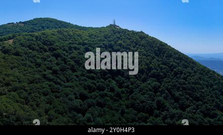 Üppig grüner Wald bedeckt Berge unter blauem Himmel mit Telekommunikationstürmen Stockfoto