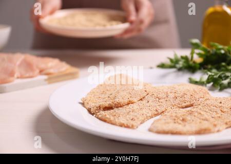 Frau, die Schnitzel am hellen Holztisch macht, konzentriert euch auf Fleischscheiben mit Brotkrümeln Stockfoto