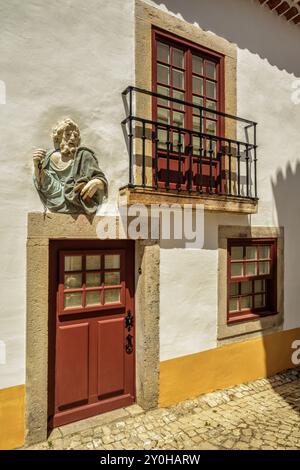 Hochrelief des Heiligen Peter mit einer Kette in der einen Hand und einem Schlüssel in der anderen an der Eingangstür eines Hauses in der mittelalterlichen Stadt Óbidos, Portugal. Stockfoto