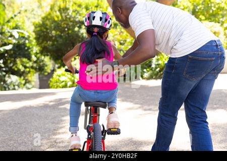 Der Vater bringt der Tochter das Fahrradfahren bei und unterstützt sie am sonnigen Tag Stockfoto