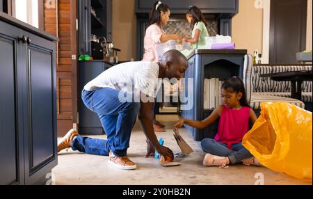 Küchenboden wird gereinigt, Vater und Tochter nehmen Müll auf, Mutter und Kind im Hintergrund Stockfoto
