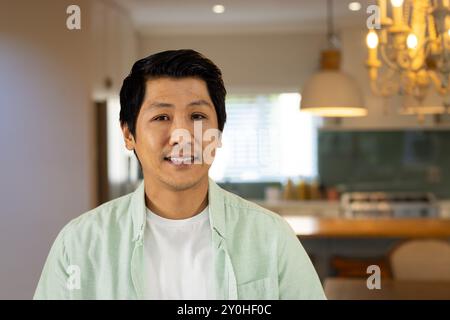 Ein lächelnder asiatischer Mann, der in einer modernen Küche steht und ein lässiges grünes Hemd trägt Stockfoto