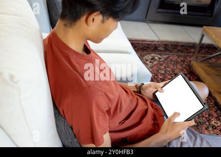 Mit Tablet, junger asiatischer Mann, der auf der Couch sitzt, Inhalte durchsucht oder liest, Kopierraum Stockfoto