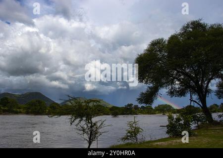 Cumuluonimbus Wolken erheben sich über dem Great Ruaha River. Am Ostufer fällt bereits Regen und am letzten Nachmittag entsteht ein Regenbogen Stockfoto