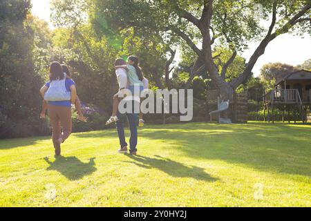 Familie trägt Töchter auf dem Rücken, läuft zusammen im sonnigen Hinterhof Stockfoto