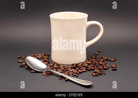 Foto von frischen Kaffeebohnen und einer cremefarbenen Tasse mit einem Teelöffel auf schwarzem Hintergrund. Stockfoto