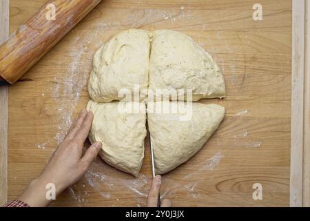 Ein flaches Foto einer Teigkugel, die auf einem großen Holzschneidebrett geschnitten wird, um es auszurollen Stockfoto