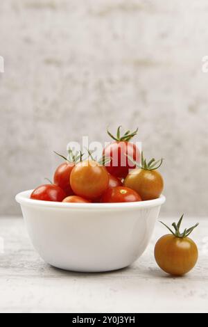 Ein Studiofoto von frischen Reifen Kirschtomaten in einer weißen Schüssel mit einer Tomate an der Seite Stockfoto