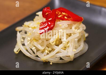 Nahaufnahme eines Stapels von Bohnensprossen, die in Fischsauce und Sesamöl gekocht wurden, mit Sesamsamen bestreut und mit drei roten Paprika garniert Stockfoto