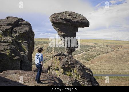 Eine junge Frau steht auf einem Felsvorsprung und blickt auf den berühmten Balanced Rock bei Buhl, Idaho Stockfoto