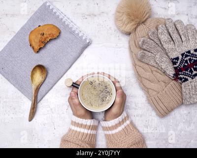 Ein flaches Foto von den Händen einer Frau, die eine Tasse Kaffee, einen Holzlöffel, Kekse, Handschuhe und einen Hut an der Seite hält Stockfoto