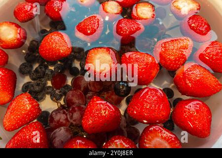 Erdbeeren, Trauben und Heidelbeeren werden in einer Schüssel Wasser gewaschen. Stockfoto