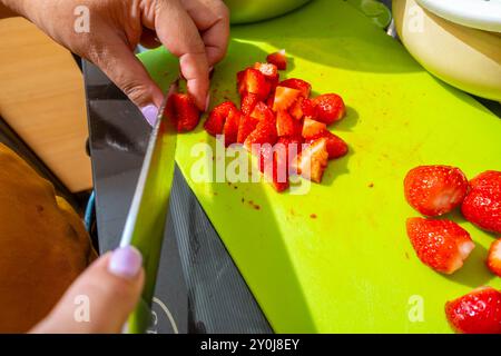 Nahaufnahme von weiblichen Händen, die Erdbeeren mit einem scharfen Küchenmesser auf einem Schneidebrett schneiden. Stockfoto