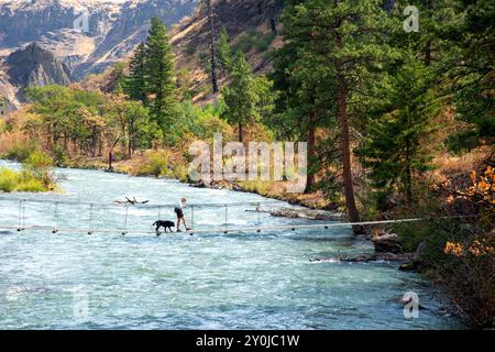 Alleinstehende Seniorin mit ihrem schwarzen Labor, die über eine Metallbrücke über dem Tieton River im Tieton River Canyon im Zentrum von Washington wandert. Stockfoto