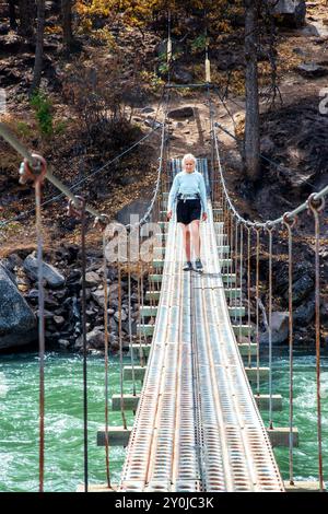 Alleinstehende Seniorin, die über eine Metallbrücke über dem Tieton River im Tieton River Canyon im Zentrum von Washington wandert. Stockfoto