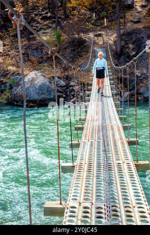 Alleinstehende Seniorin, die über eine Metallbrücke über dem Tieton River im Tieton River Canyon im Zentrum von Washington wandert. Stockfoto