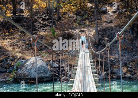 Alleinstehende Seniorin, die über eine Metallbrücke über dem Tieton River im Tieton River Canyon im Zentrum von Washington wandert. Stockfoto