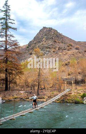 Alleinstehende Seniorin mit ihrem schwarzen Labor, die über eine Metallbrücke über dem Tieton River im Tieton River Canyon im Zentrum von Washington wandert. Stockfoto