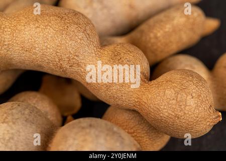 Geschlossene, lange reife Tamarindenschoten aus der Nähe, verzehrfertige ganze Tamarindenfrüchte liegen auf dem Tisch Stockfoto