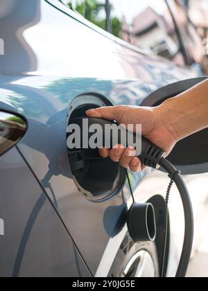 Mann, der sein Elektroauto auflädt. Nahaufnahme des Einsteckens des elektrischen Steckverbinders am Fahrzeug. Stockfoto