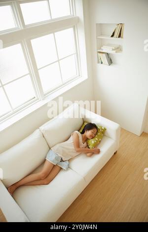 Mädchen, das auf dem Sofa am Fenster liegt, von oben genommen Stockfoto