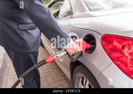 Person, die Gas pumpt. Benzin für das Auto an der Tankstutzen im Tank. Hand und rote Tankpistole aus nächster Nähe. Stockfoto