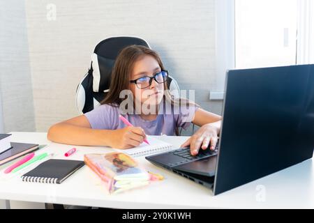 Teenager-Schülerin, die online von zu Hause aus studiert und Notizen macht. Teenager-Schüler Fernunterricht auf Laptop Hausaufgaben machen, Video anschauen Stockfoto