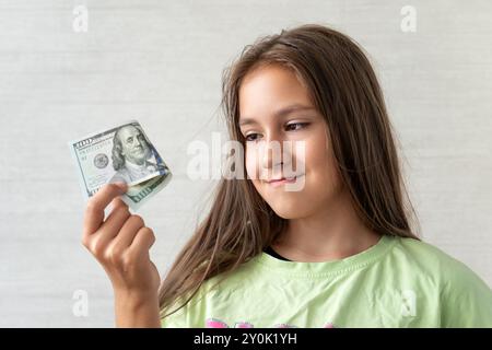 Fröhliches Teenager-Mädchen, das lächelnd ist, hält einen Stapel von Hundert-Dollar-Scheinen auf weißem Hintergrund Stockfoto