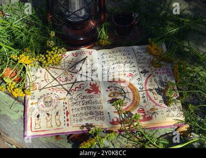 Mystisches Stillleben mit Zauberbuch und heilenden Kräutern und Blumen auf dem alten Tisch. Okkultes, esoterisches, Wicca- und Wahrsagungskonzept. Kein fremdes lan Stockfoto