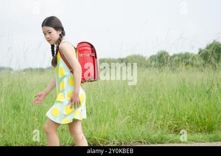 Mädchen, das einen Rucksack auf dem Rücken trägt und an einem grasbewachsenen Ort Stockfoto