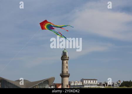 Blick am Mittwoch 14.08.2024 im Ostseebad Warnemünde, ein Ortsteil der Hanse- und Universitätsstadt Rostock, bei sommerlichem Wetter auf den historischen Leuchtturm während davor ein Tourist einen Drachen steigen lässt. In den Urlaubsorten entlang der Ostseeküste des Landes Mecklenburg Vorpommern herrscht derzeit reges Treiben. In direkter Strandnähe ist fast kein freier Platz mehr zu finden und die Restaurants sind gut besucht. Dennoch bleibt ein Wermutstropfen. Die Preise in den Tourismusregionen des Landes MV sind in diesem Jahr noch einmal gestiegen. Das hält zahlreiche Menschen aber nic Stockfoto