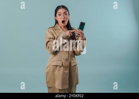 Schockierte Regierungsangestellte in Khaki-Uniform und Brille, die ihr Handy hält und auf sie zeigt. PNS-Beamtenkonzept. Stockfoto