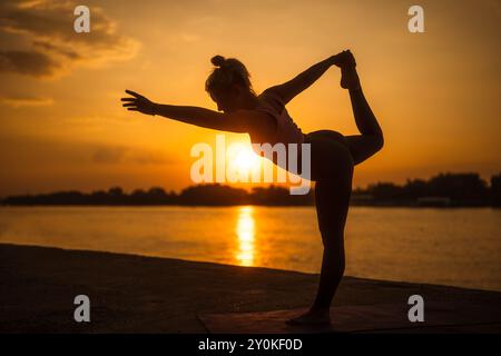 Frau übt Yoga bei Sonnenuntergang. Natarajasana/Shiva-Haltung Stockfoto