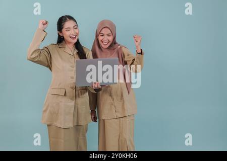 Zwei freudige Regierungsangestellte in Khaki-Uniform, die einen Laptop mit einem glücklichen, erfolgreichen Ausdruck hält. PNS und Beamtenkonzept. Stockfoto