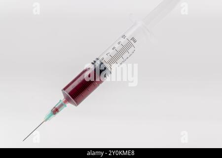 Nahaufnahme einer Spritze mit Blut, geneigt und zentral im Bild platziert. Die horizontale Ausrichtung und der weiße Hintergrund heben die s hervor Stockfoto