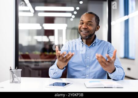 Selbstbewusster Geschäftsmann lächelt und gibt Gesten während eines Bürogesprächs. In lässiger Kleidung strahlt er Freundlichkeit und Professionalität aus. Stockfoto