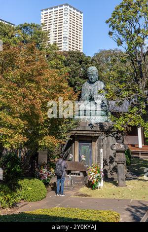 Ein junger Mann betet an einer buddhistischen Statue in einem Park in tokio Stockfoto