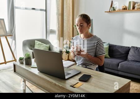 Eine junge Frau genießt einen ruhigen Moment mit einem warmen Getränk an ihrem Schreibtisch. Stockfoto