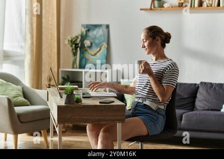 Eine lächelnde Frau mit Vitiligo schlürft Kaffee, während sie sich mit ihrem Laptop beschäftigt. Stockfoto