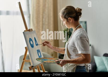 Eine Frau mit Vitiligo malt zart blaue Formen auf ihre Leinwand. Stockfoto